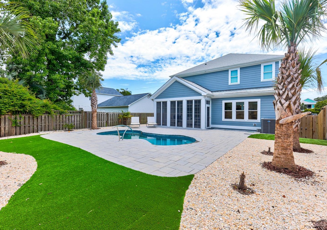 A coastal-inspired home with a private pool nestled in a landscaped backyard featuring palm trees, lush lawn, and a spacious patio perfect for sunny afternoons.