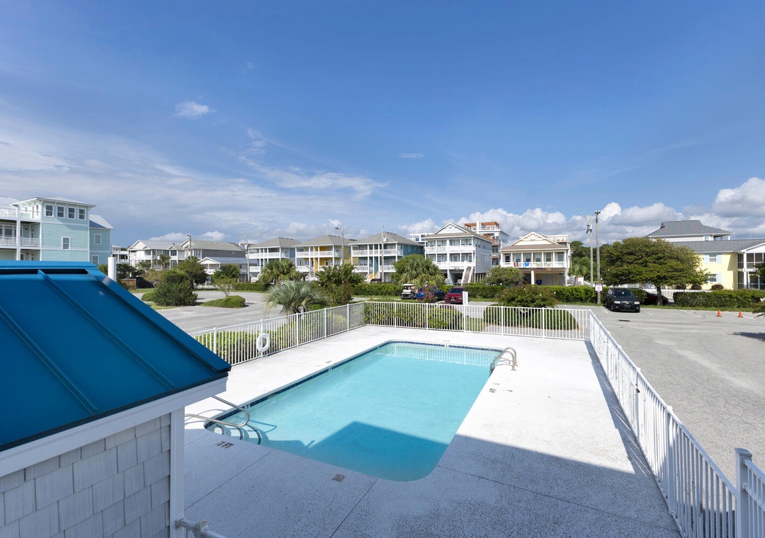 A peaceful beachside community surrounds the property, with colorful coastal homes and lush greenery creating a charming vacation atmosphere beneath a bright sunny sky.