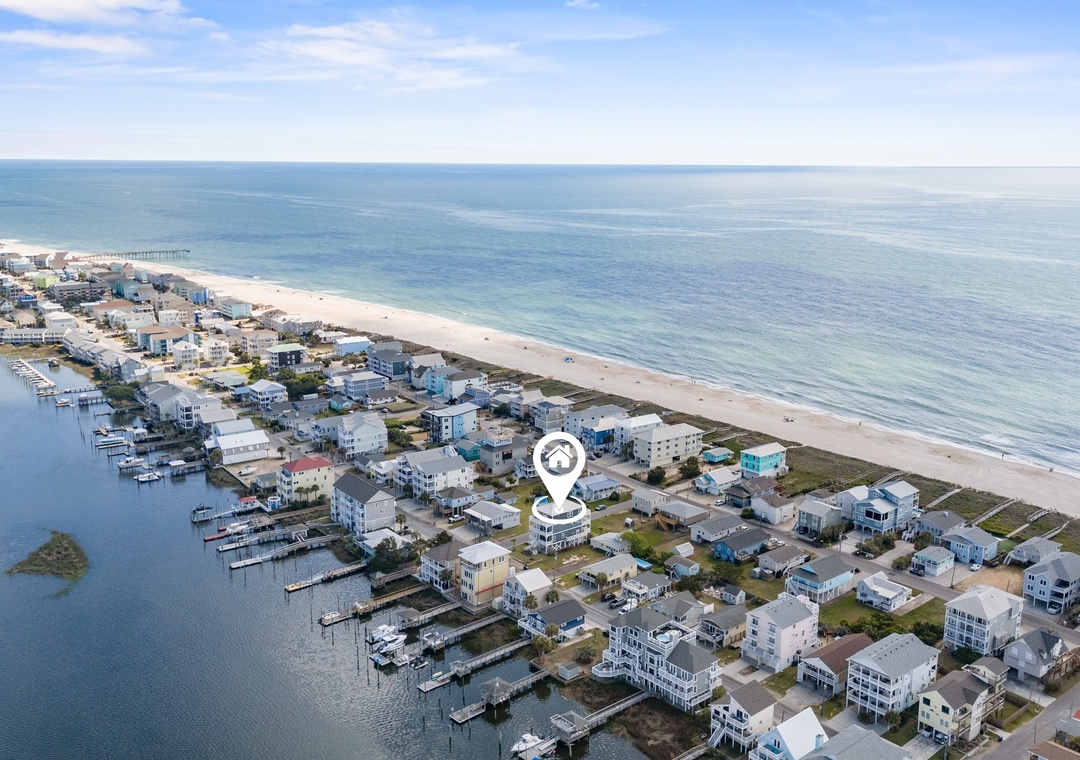 Aerial view of a beachfront coastal community with waterfront access, sandy shores, and calm ocean waters under clear blue skies.
