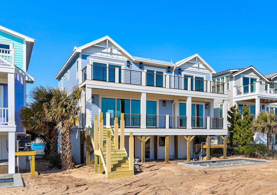 Modern beach house elevated on stilts with expansive balconies and direct beach access via wooden walkway.