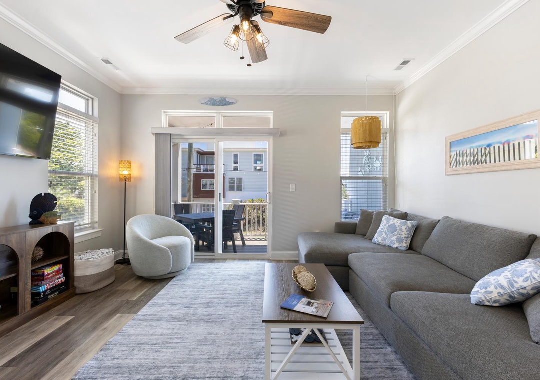 Relax in your open, sun-filled living room with plush seating, coastal touches, and glass doors opening to a private balcony for fresh air and easy flow.