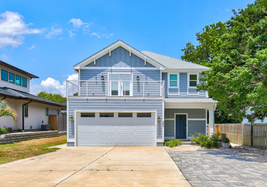 A charming coastal-style property featuring modern blue siding, a spacious second-story balcony, and welcoming covered entrance. The home sits in a peaceful residential neighborhood with ample parking and attractive landscaping.