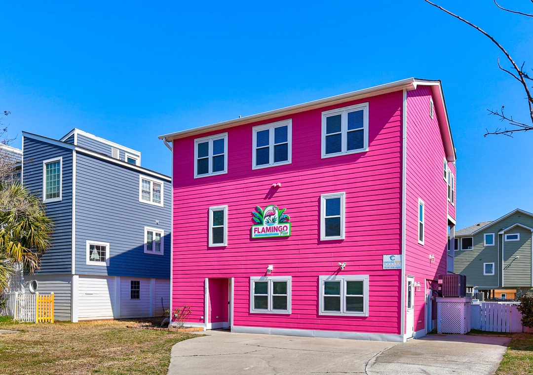 Vibrant pink beach house stands out in the coastal neighborhood with distinctive Flamingo branding and classic beach architecture.