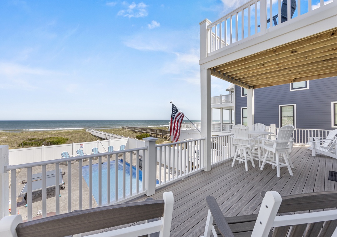 Beachfront property featuring expansive outdoor decks with white railings and seating areas, offering direct coastal access and ocean views.