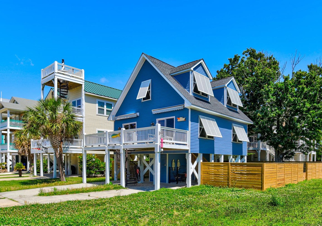 Charming coastal rental with vibrant blue siding, elevated design, and spacious balconies set in a sunny, palm-lined neighborhood perfect for a beach getaway.