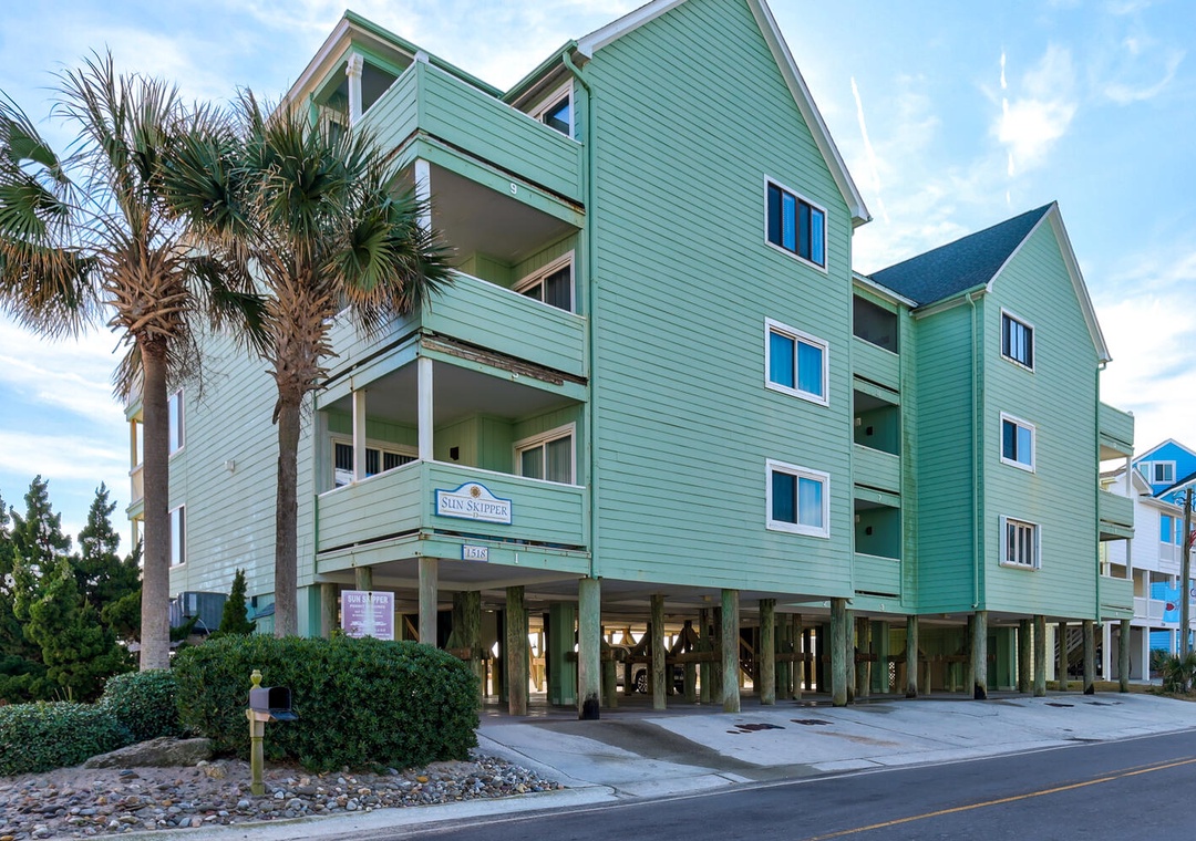 Coastal charm awaits at this distinctive green beach house with multiple levels and tropical palm trees.
