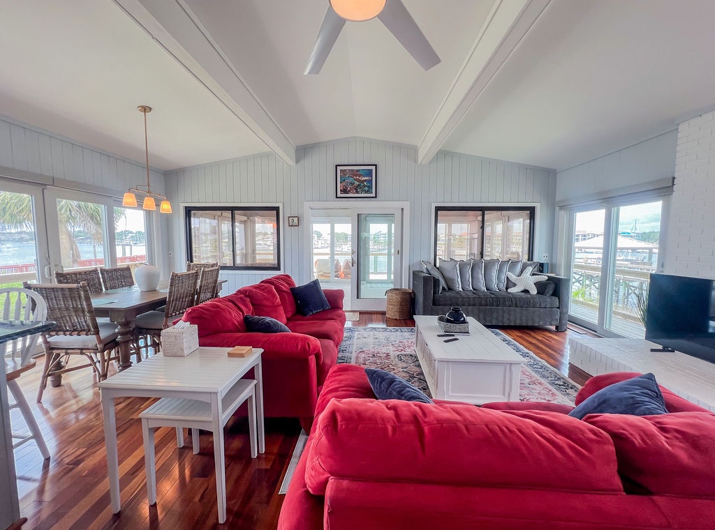Sink into plush seating as natural light floods your open living space, where vibrant red sofas meet elegant dining areas—all framed by stunning marina views through every window.