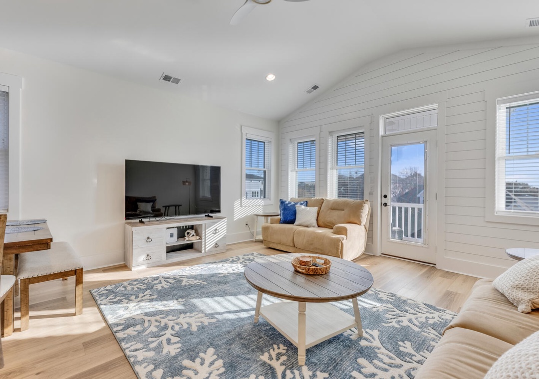 Sink into plush sofas in your bright living space, where natural light streams through multiple windows and a coastal-themed rug adds charm to your relaxing retreat.