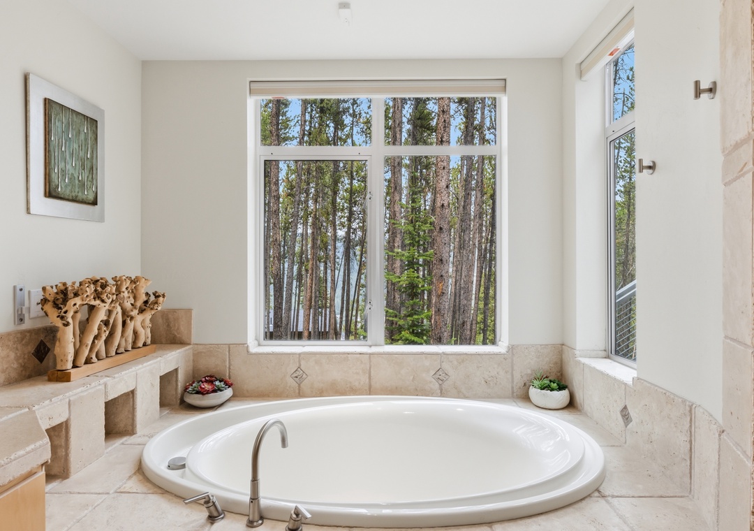 Soak in serenity with tall forest views framing your private tub retreat. Clean lines, natural light, and warm stone surround you in comfort, while nature calms your senses right outside the window.