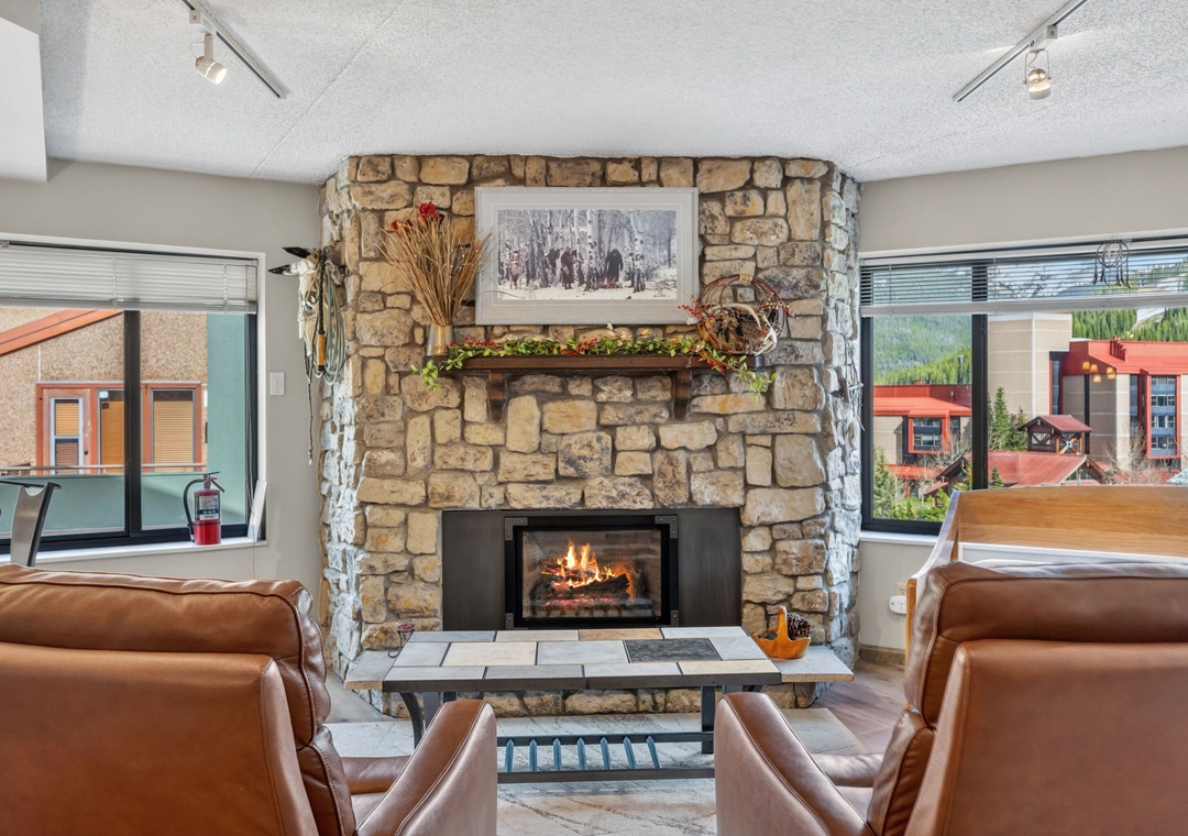 Settle into plush leather seating by a warm stone fireplace, where rustic mountain charm meets modern comfort in your inviting communal lounge space.
