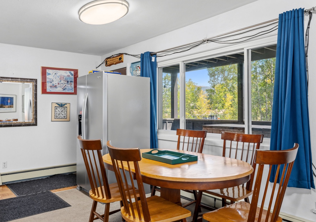 This bright dining area features a welcoming round table surrounded by wooden chairs and a full-sized refrigerator.