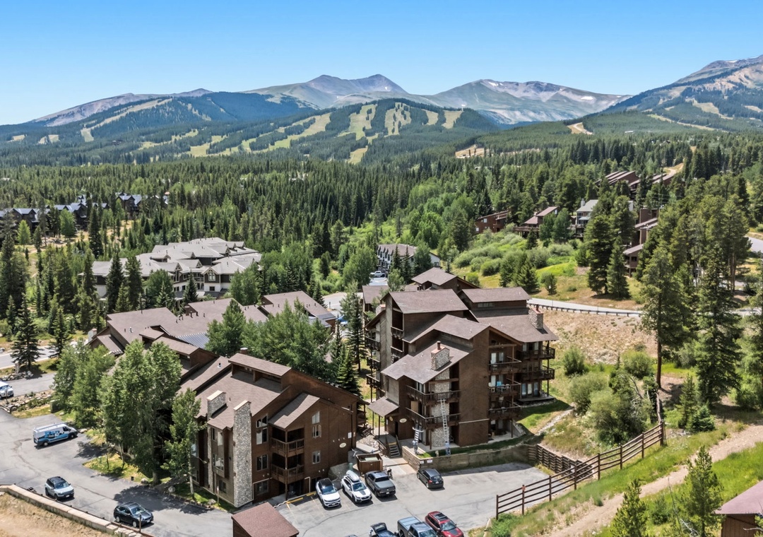 Nestled in a stunning mountain community surrounded by alpine peaks and evergreen forests, with ski slopes visible on the ridges above and peaceful natural beauty all around.