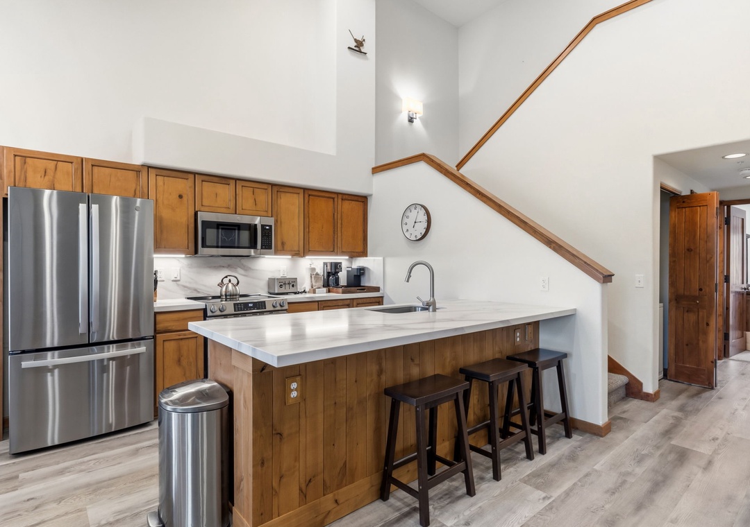 Your full kitchen features stainless steel appliances, warm wood cabinetry, and a bright island with seating—perfect for gathering over morning coffee or prepping meals together.