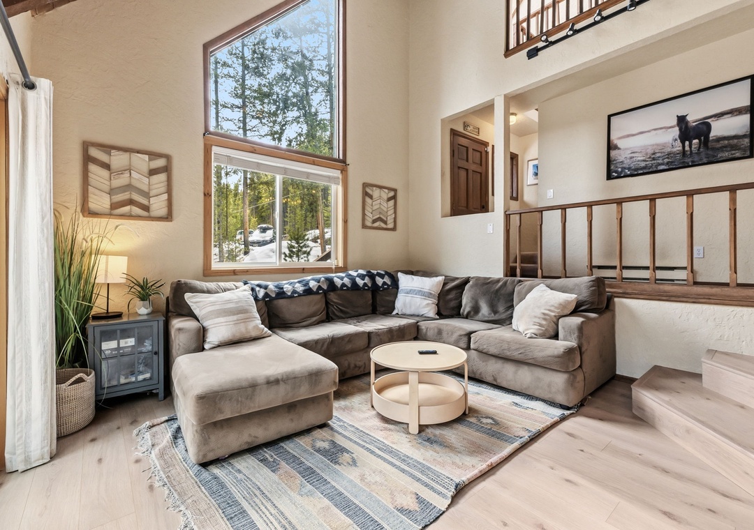 Unwind on the plush sectional sofa while natural light streams through soaring windows, creating your perfect mountain retreat sanctuary.