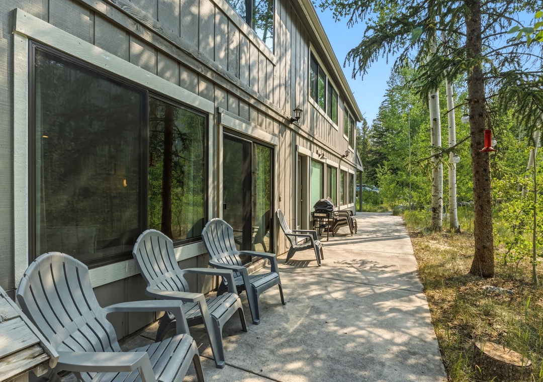 The property sits nestled among towering pines and natural greenery, offering a peaceful wooded retreat with modern architecture and shaded outdoor seating areas.