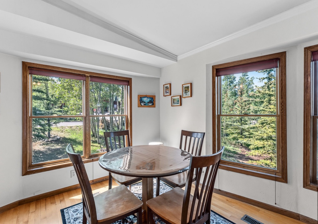 Enjoy your morning coffee at this inviting dining table surrounded by natural light and peaceful woodland views through three large windows that bring the outdoors in.