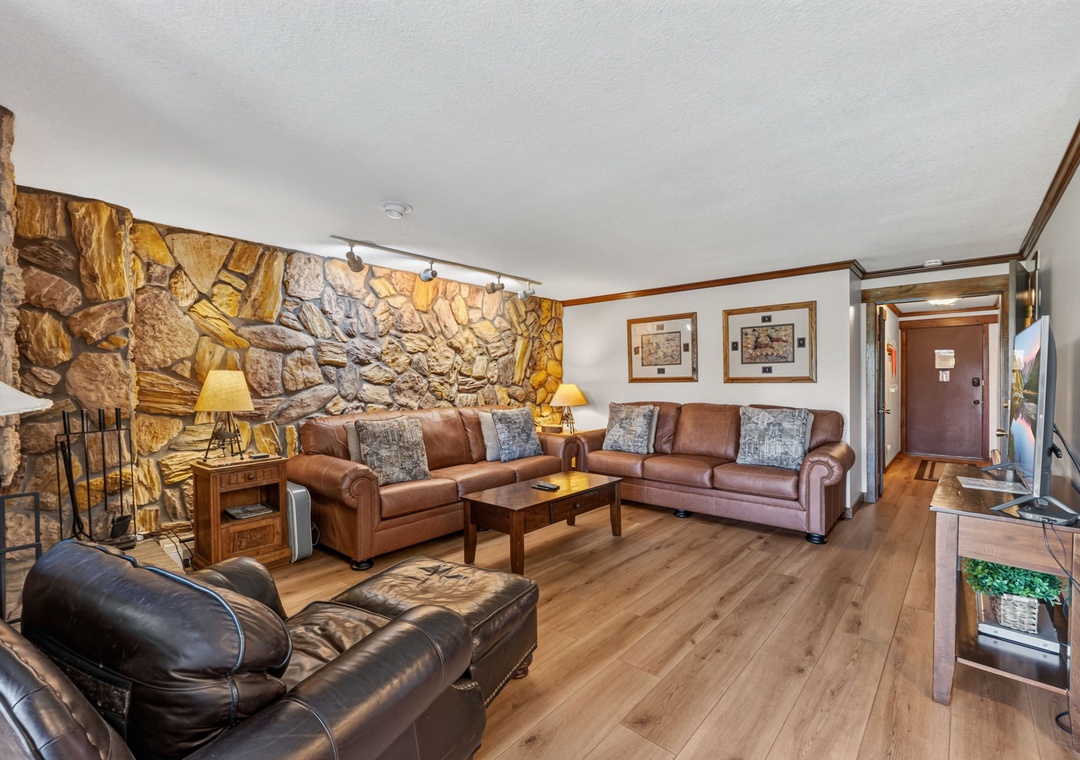 Relax in your rustic yet elegant living space, where warm wood floors, natural stone fireplace, and comfortable leather seating create a cozy mountain retreat perfect for unwinding after your adventures.