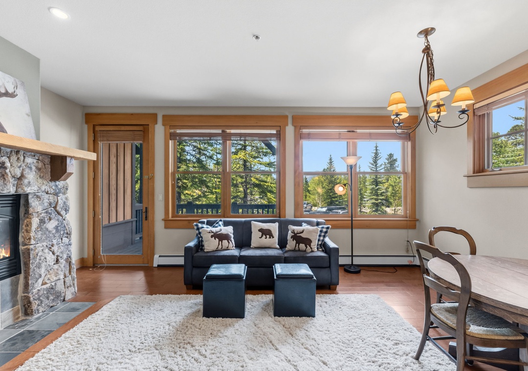 Sink into comfort with stunning forest views through expansive windows. Your cozy living space features a stone fireplace and inviting seating—perfect for unwinding after a day of mountain adventure.