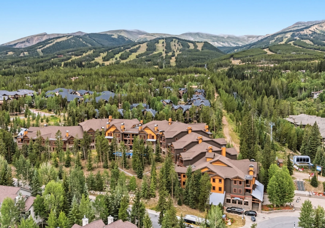 An aerial view showcasing the mountain resort property nestled among evergreens, with expansive ski slopes and forested valleys stretching into the distance.