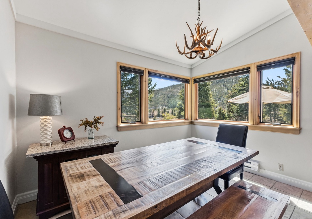 Gather around this handcrafted dining table beneath a striking antler chandelier and soak in the forested mountain scenery through expansive corner windows—perfect for morning coffee or evening wine.