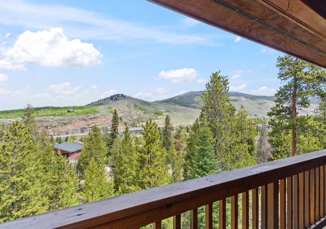 The property offers scenic views of rolling mountain terrain, evergreen forests, and nearby residential areas framed by a covered outdoor space.