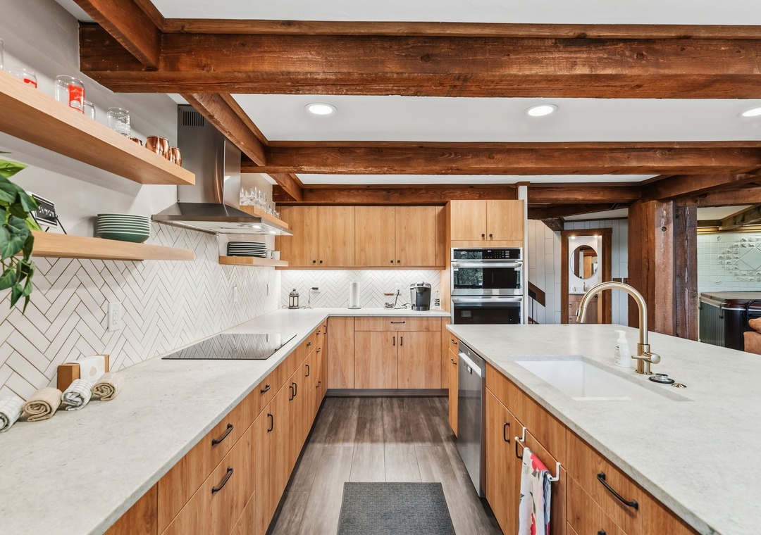 You'll love preparing meals in this inviting kitchen, where warm wood tones and modern quartz countertops blend beautifully beneath rustic exposed beams, making every cooking moment feel like home.
