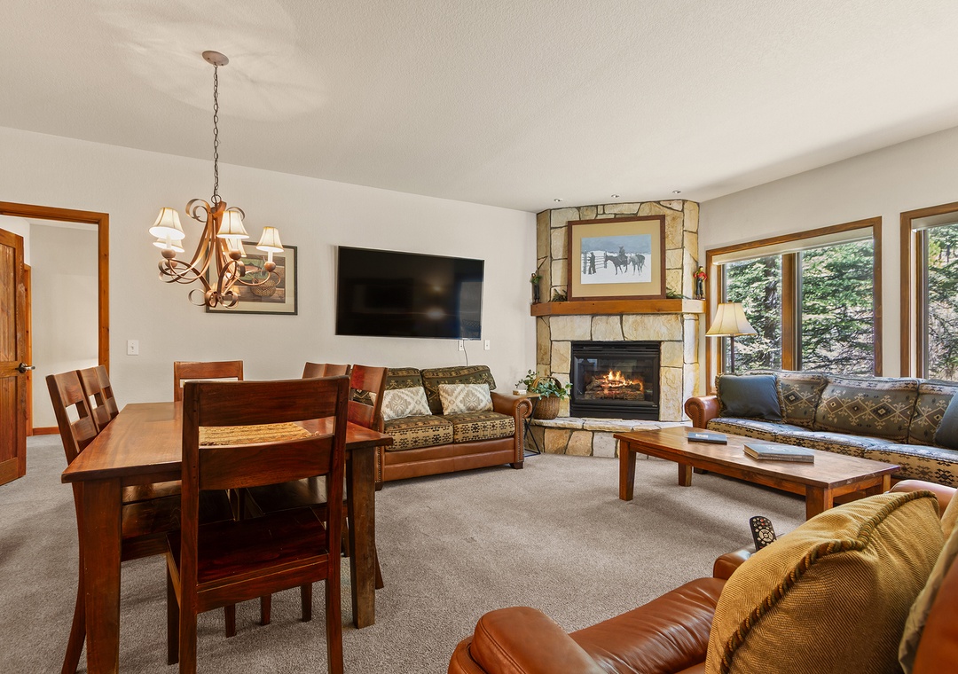 Warm up by your fireplace in this cozy living area with comfortable seating, a dining table for meals, and views of evergreens through large windows.