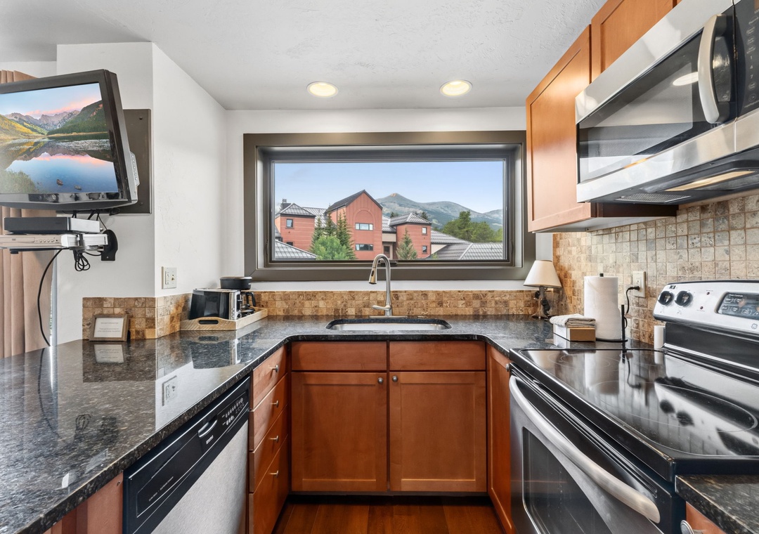 Your fully-equipped kitchen features sleek granite countertops, modern stainless steel appliances, and a window framing peaceful mountain views—perfect for preparing meals while soaking in the scenery.