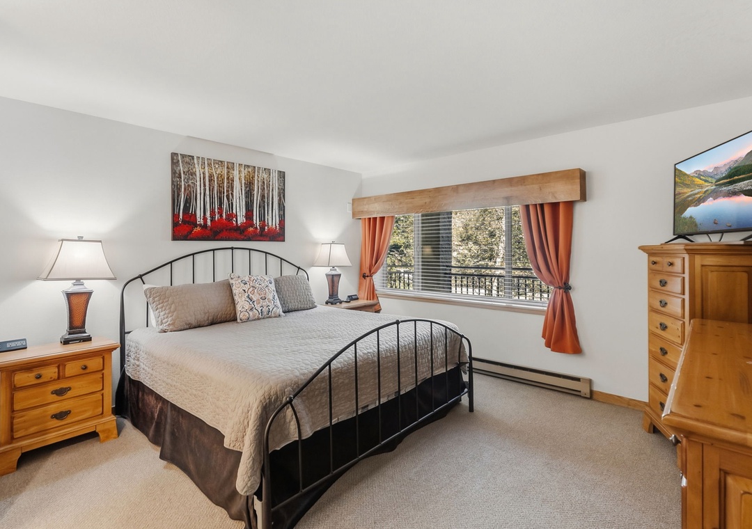 Sink into your peaceful retreat featuring a cozy queen bed, charming wooden furnishings, and natural light streaming through the window.