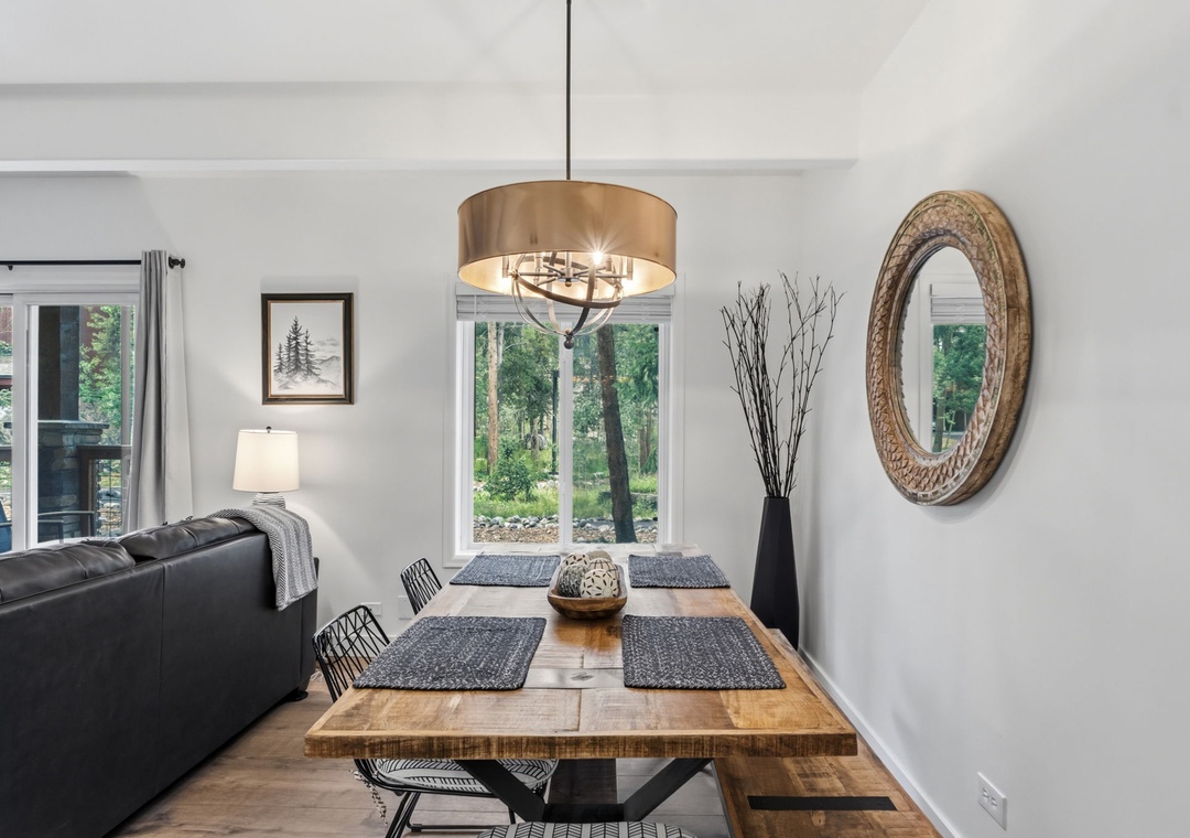 Gather around a beautifully crafted dining table set for your meals, with natural light pouring through large windows framing peaceful wooded views.