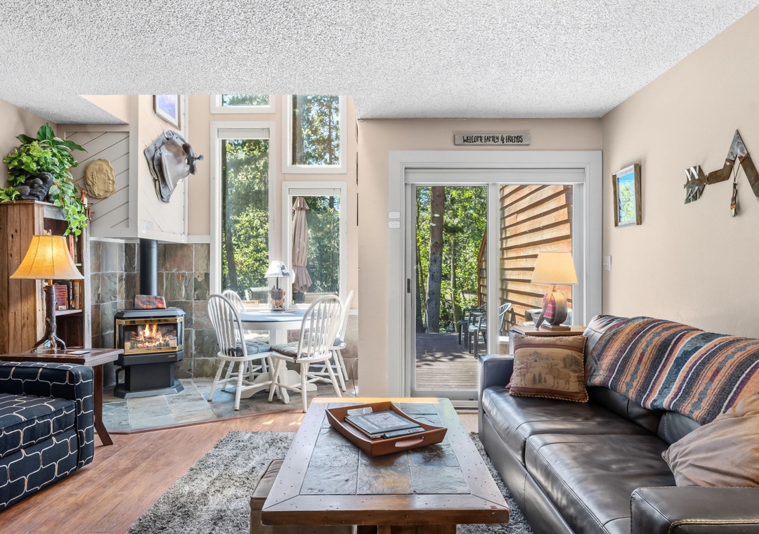 Relax in this cozy living space with a warm fireplace and large windows framing lush forest views. Step onto your private deck to enjoy the peaceful surroundings.
