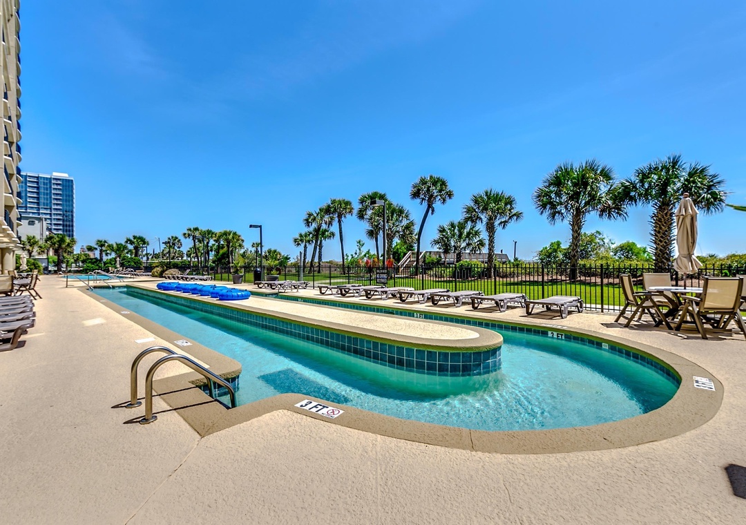 Dive into your private oasis! This sparkling lazy river pool beckons you to float away your worries under the brilliant blue sky, surrounded by swaying palms and endless sunshine.