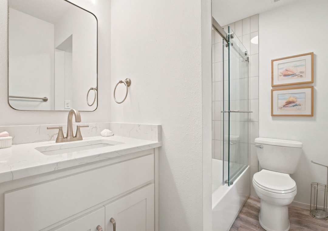 Gulfside Villas 2B- Your bright, freshly updated bathroom features clean marble countertops, a spacious walk-in shower with a sleek glass enclosure, and coastal artwork that sets a relaxing, beachy tone for your stay.