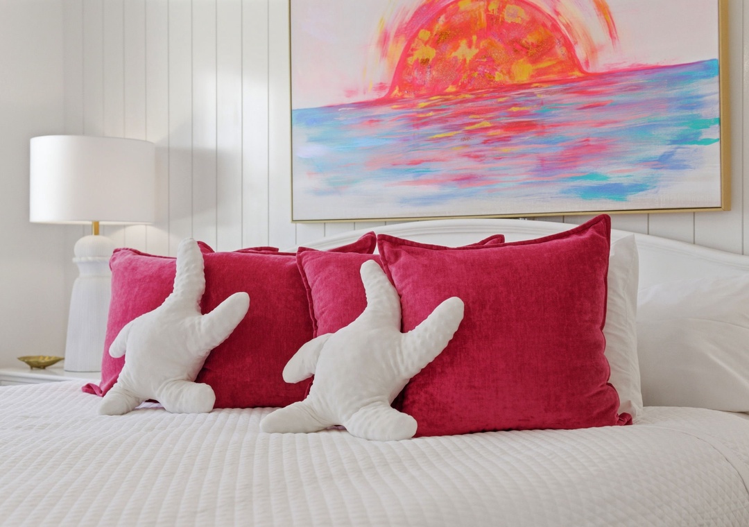 North Lost Key Landing B2- Sink into crisp white linens and vibrant magenta pillows beneath a stunning sunset painting. Two playful starfish accent pillows invite you to unwind in this coastal-inspired retreat.
