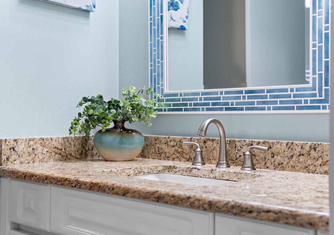 Beach Colony Tower 10C- Refresh in your stylish bathroom with its granite countertop and coastal-inspired tile mirror. The soothing blue palette and fresh greenery create a spa-like retreat.
