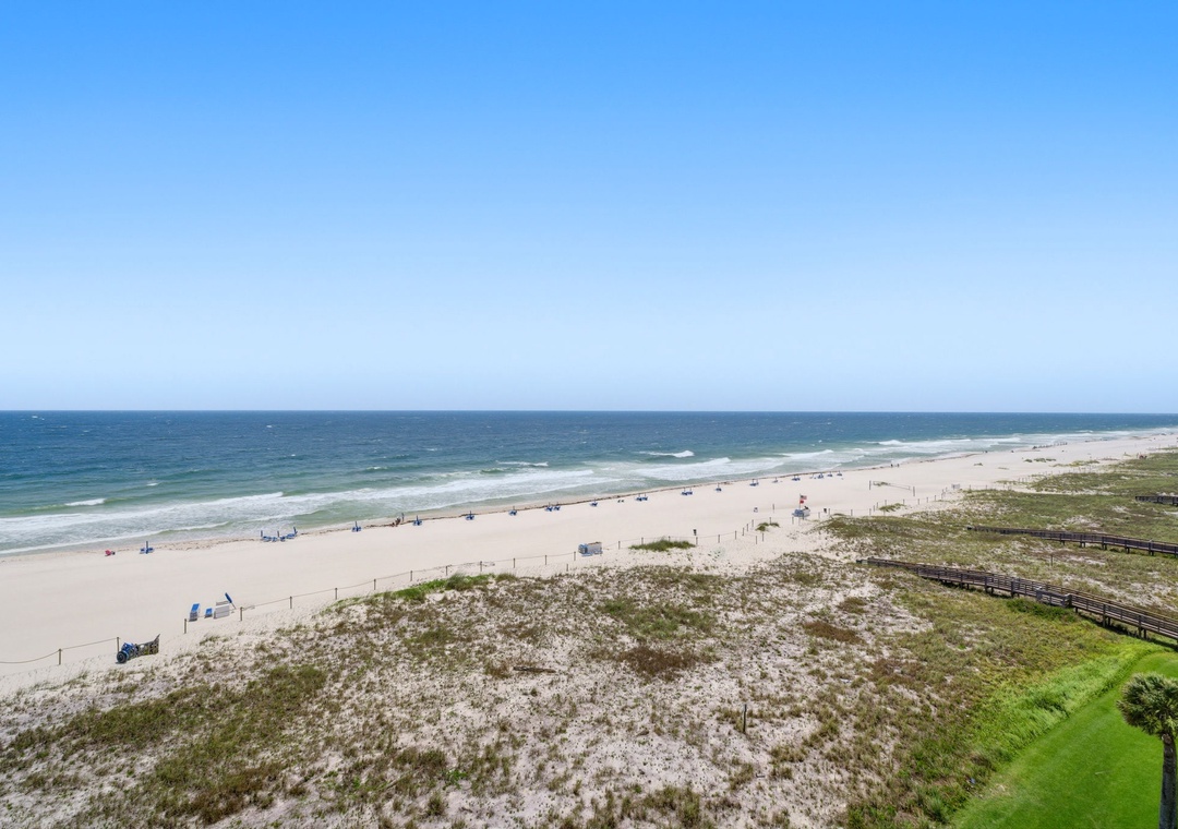 Shipwatch D803- Stunning aerial perspective of pristine beachfront, showcasing white sands, gentle waves, and natural dune vegetation along the coastline under clear skies.