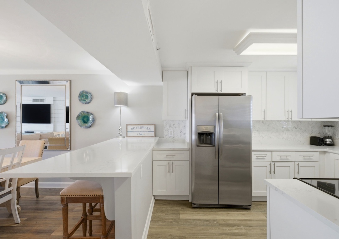 Sandy Key 827- A bright, modern kitchen invites you to cook and gather, featuring sleek white cabinetry, marble backsplash, stainless appliances, and a spacious island perfect for meals or conversation.