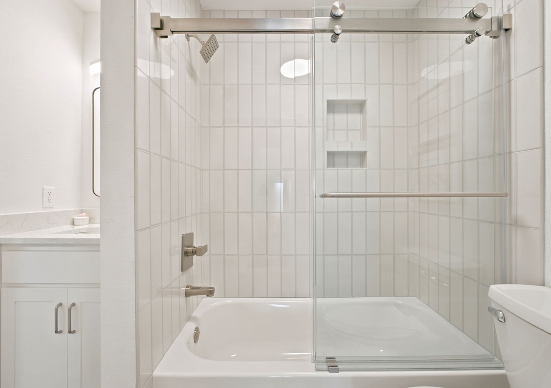 Gulfside Villas 2B- Crisp white tiles line your spa-inspired bathroom with a dual-head rainfall shower, deep soaking tub, and glass enclosure for a fresh, modern retreat.