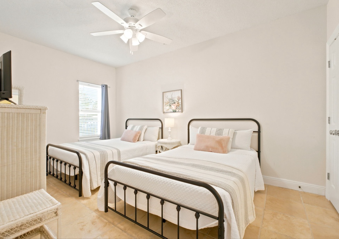 Two soft beds await in this peaceful guest room, where a ceiling fan keeps you comfortable and natural light flows through the window, ready for a restful stay.