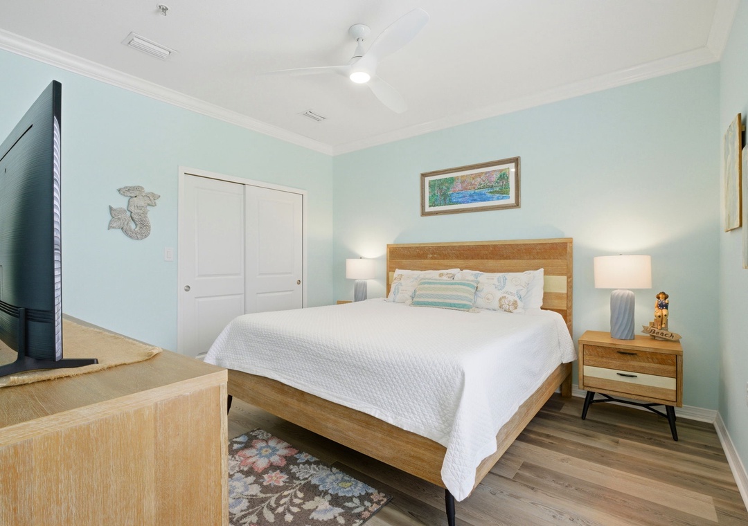 Your serene bedroom retreat features a plush queen bed, coastal decor, soothing aqua walls, and modern amenities like a ceiling fan and flat-screen TV for ultimate comfort.