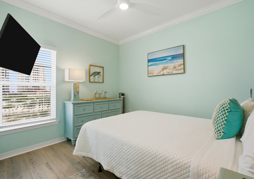 Unwind in your coastal-inspired retreat featuring a plush bed, serene aqua walls, and calming beach artwork that invites peaceful nights and refreshing mornings.