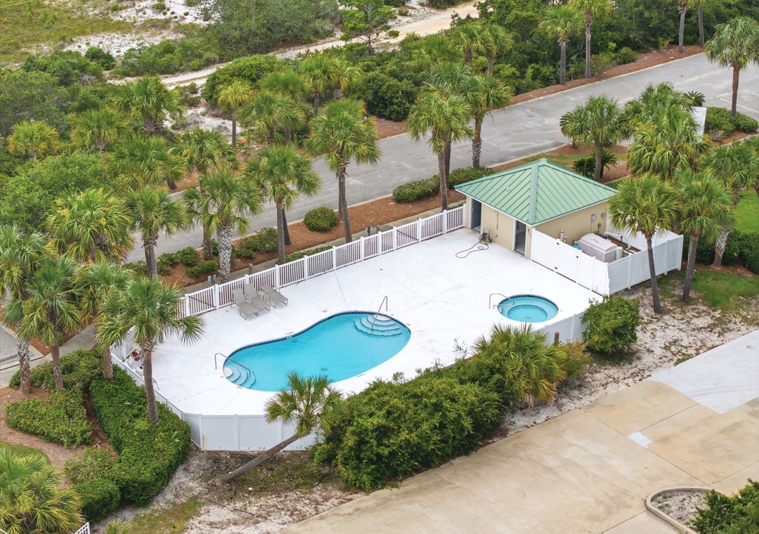 Aerial view of the property showcasing a refreshing pool with spa, surrounded by tropical landscaping and palm trees, with convenient parking and beach access paths nearby.