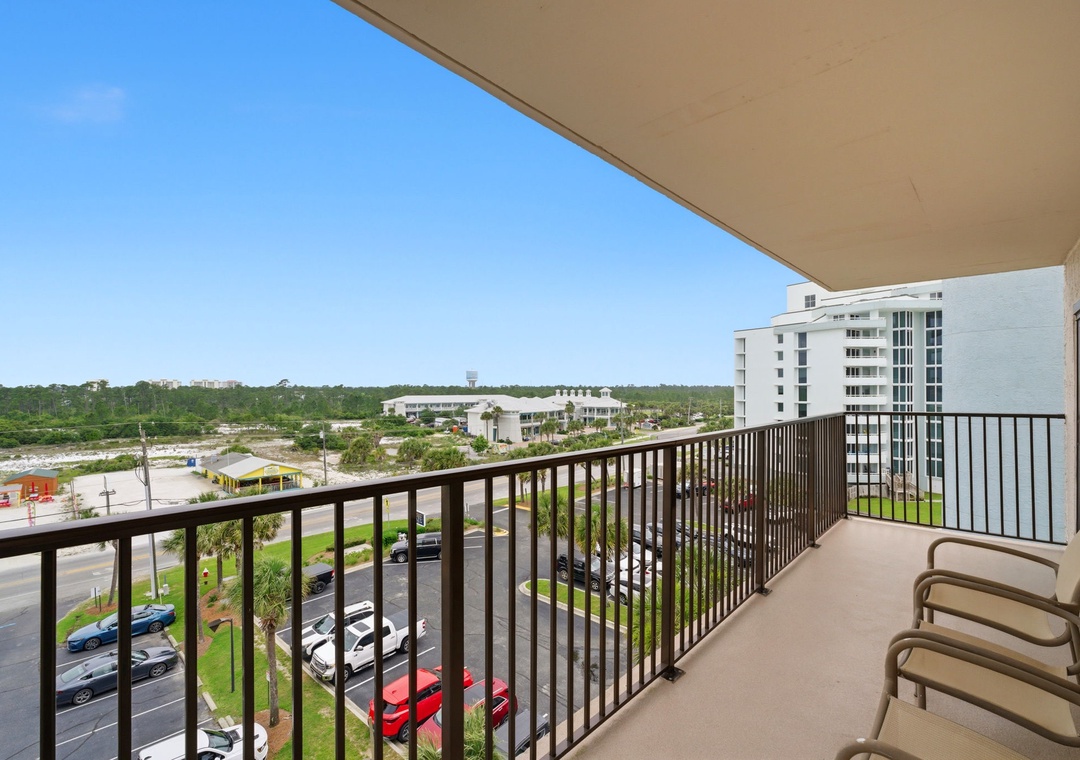 Ocean Breeze E601- A private balcony offering sweeping views of the surrounding area, with nearby buildings and greenery visible under a clear blue sky.