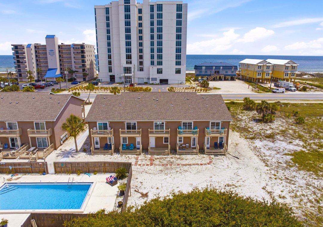 Aerial view of beachfront property showing rental units with private balconies, a communal pool, and direct access to sandy shores and ocean views.