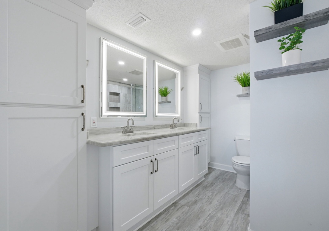 Step into this spa-like bathroom with dual vanities, ambient lighting, and modern finishes. The bright, clean space with fresh greenery creates a serene start to your mornings.