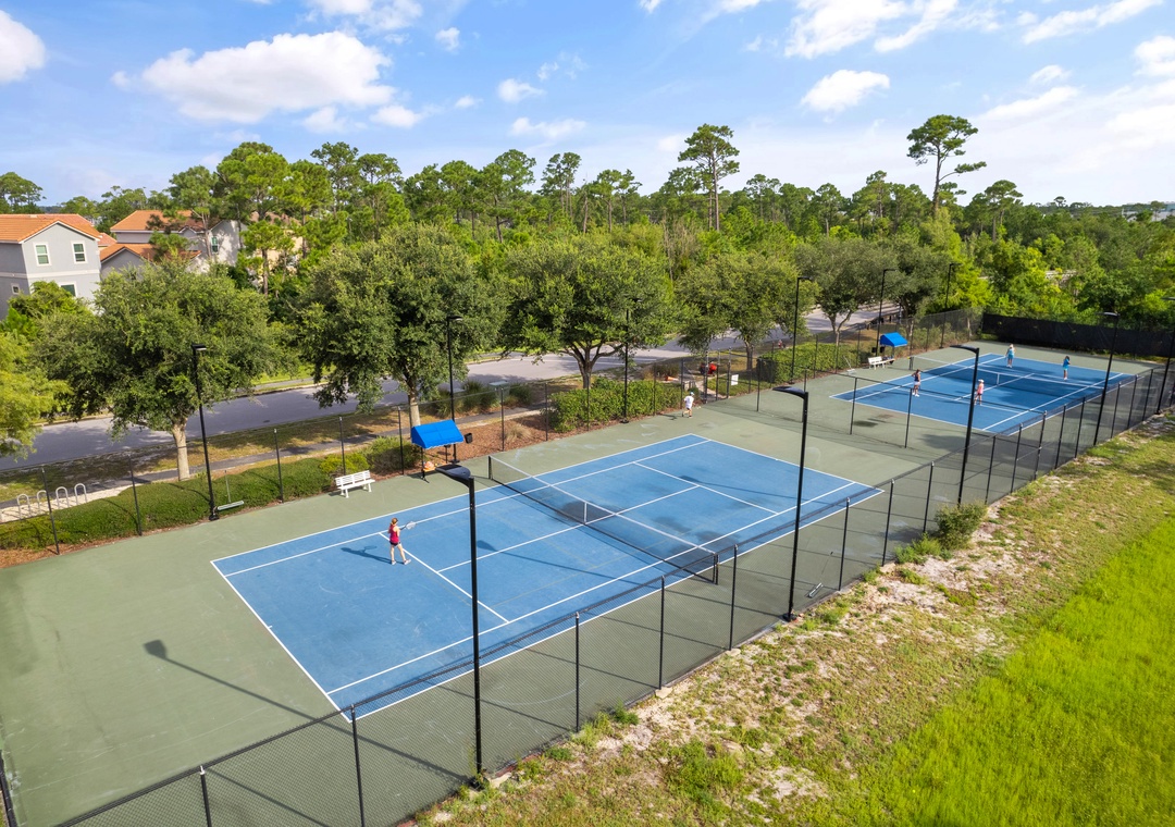 Lost Key Community Two professional tennis courts with bright blue surfaces sit within the residential community, surrounded by lush greenery and shaded seating areas.