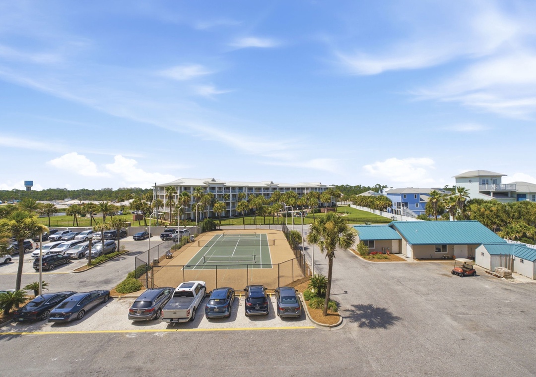Sandy Key 411- Elevated view of the property showcasing tennis courts, ample parking, and tropical landscaping with palm trees spread across the grounds.