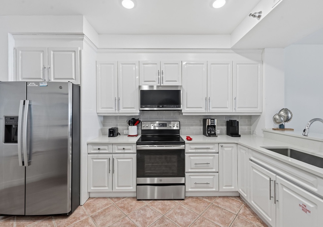 Beach Colony T14B- Cook with ease in this bright, fully-equipped kitchen featuring modern stainless steel appliances, sleek white cabinetry, and plenty of counter space for preparing your favorite meals.