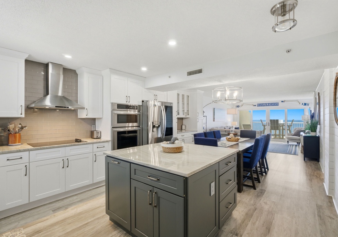 Cook with ocean views in this bright, modern kitchen featuring a spacious island, stainless steel appliances, and elegant white cabinetry. Gather around the island and enjoy coastal breezes flowing through your open living space.