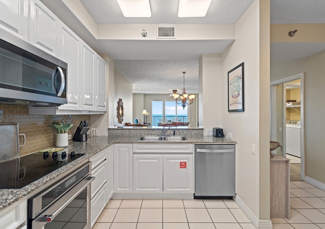 Beach Colony T15B- Step into your fully-equipped kitchen where gleaming countertops and modern appliances make meal prep a breeze, with glimpses of ocean blue calling from beyond.